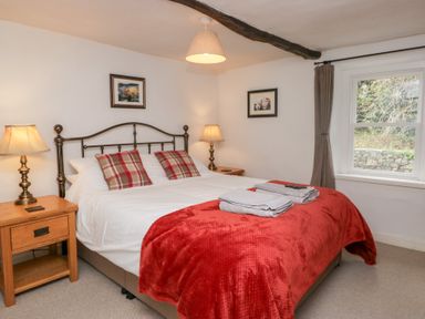 A bedroom with a double bed with two plaid pillows and a red blanket two bedside tables with lamps and two framed pictures on the walls at Latch Cottage in Keswick