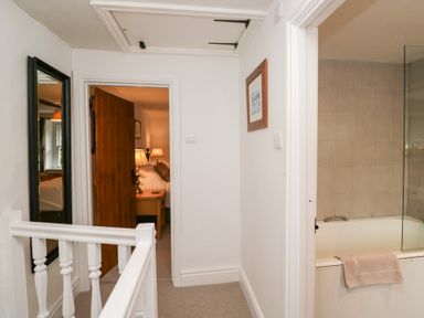 A hallway with a bathroom on the right and a bedroom visible through an open door at Latch Cottage in Keswick