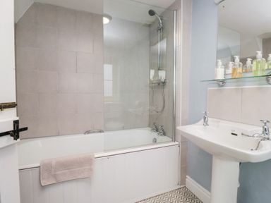 A bathroom with a bathtub shower combination a sink with soap dispensers and a towel on the bathtub at Latch Cottage in Keswick