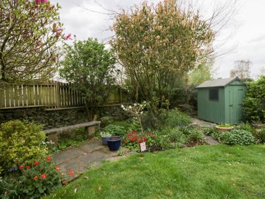 A garden with grass a stone bench flower pots and a green shed at Latch Cottage in Keswick