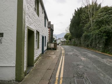 A narrow street with white stone houses on the left and trees with stone walls on the right at Latch Cottage in Keswick