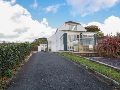 A driveway leading to a two-story house with a glass balcony and plants on the side at Seacroft in Crantock