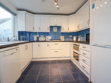 A kitchen with white cabinets blue tiled walls a dishwasher oven microwave and refrigerator at Seacroft in Crantock