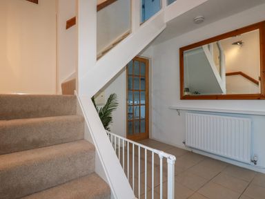 A stairway with beige carpet and white railing next to a hallway with a wooden framed mirror radiator and a wooden door at Seacroft in Crantock