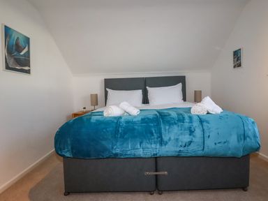 A bedroom with a double bed with white pillows and a blue blanket with two bedside tables and lamps at Seacroft in Crantock
