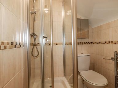 A bathroom with a glass shower enclosure a toilet and tiled walls at Seacroft in Crantock
