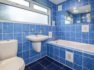 A bathroom with blue tiles a white toilet a wall-mounted sink and a bathtub with a mirror above the tub at Seacroft in Crantock