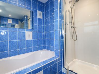 A bathroom with a bathtub and a shower cubicle with blue tiled walls at Seacroft in Crantock