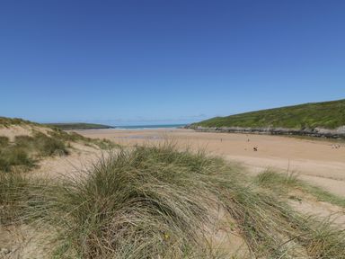 A sandy beach with dune grass and hills in the background at Seacroft in Crantock
