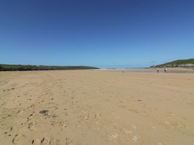 A sandy beach with footprints and a few people walking near the water at Seacroft in Crantock