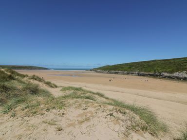 A sandy beach with grassy dunes and hills in the background at Seacroft in Crantock