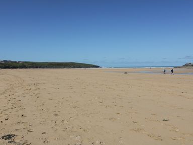 A sandy beach with a few people walking and green hills in the distance at Seacroft in Crantock