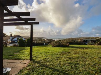 A grassy yard with a gazebo frame and houses on a hill with ocean and cloudy sky in the background at Seacroft in Crantock