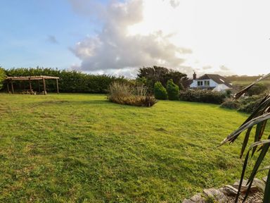 A grassy backyard with bushes a wooden pergola and a house in the distance at Seacroft in Crantock