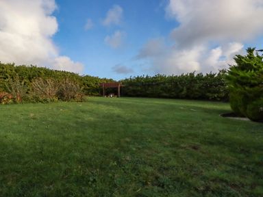 A grassy backyard with bushes around the edges and a wooden pergola with a picnic table at Seacroft in Crantock
