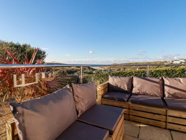 An outdoor seating area with wooden furniture and cushions overlooking a coastal landscape