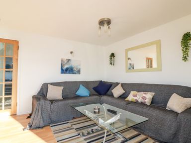 A living room with a gray sofa covered in fabric pillows and a glass coffee table on a striped rug at Seacroft in Crantock