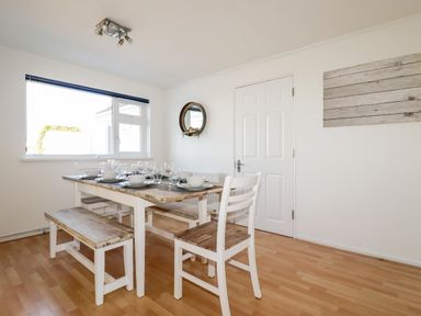 A dining room with a wooden table set with dishes and glassware and wooden chairs at Seacroft in Crantock