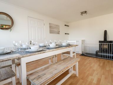 A dining room with a wooden table set with bowls glasses and plates a wood stove with a safety gate and a round mirror on the wall at Seacroft Crantock