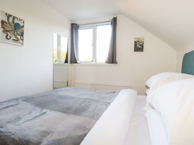 A bedroom with a bed white pillows gray blanket window with curtains mirror and wall art at Seacroft in Crantock
