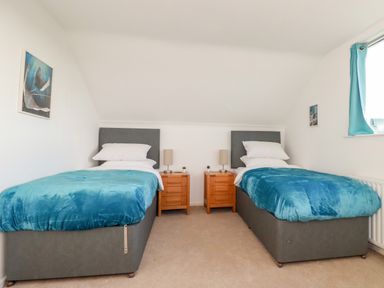 A bedroom with two single beds blue blankets gray headboards two wooden nightstands with lamps and a window with blue curtains at Seacroft Crantock