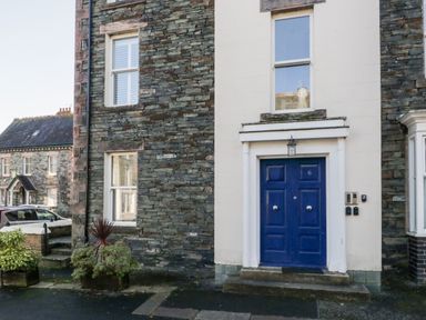 The entrance of a stone house with a blue door and two windows at Carlton House Apartment 1 in Keswick