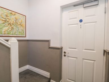 A hallway corner with a white door numbered 1 a map on the wall and gray wainscoting at Carlton House Apartment 1 in Keswick