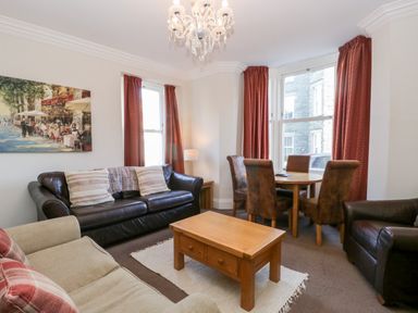 A living room with sofas a wooden coffee table and dining table with chairs at Carlton House Apartment 1 in Keswick