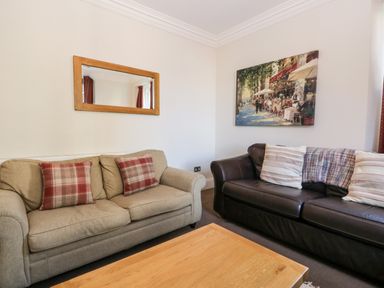A living room with two sofas a wooden coffee table a wall mirror and a painting at Carlton House Apartment 1 in Keswick
