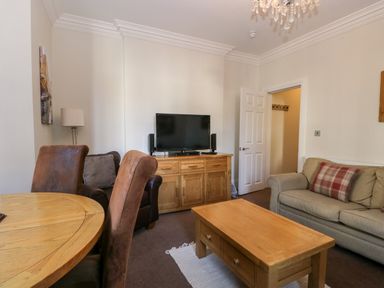 A living room with a wooden coffee table a TV on a wooden cabinet armchairs and a sofa with a plaid pillow at Carlton House Apartment 1 Keswick