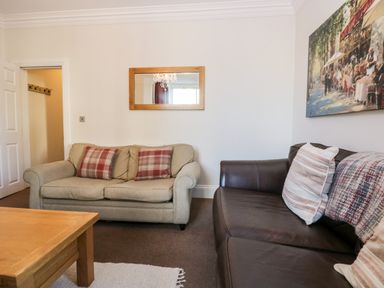 A living room with two sofas a wooden coffee table a wall mirror and a painting at Carlton House Apartment 1 in Keswick