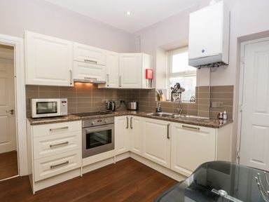 A kitchen with white cabinets a microwave oven stove toaster kettle and a sink at Carlton House Apartment 1 in Keswick