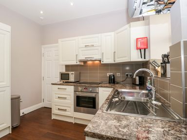 A kitchen with white cabinets stainless steel oven and microwave and a sink at Carlton House Apartment 1 in Keswick