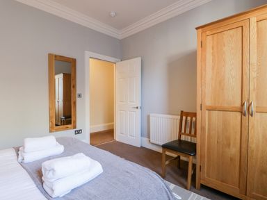 A bedroom with a bed with towels on it a wooden wardrobe a wooden chair a wall mirror and an open door at Carlton House Apartment 1 in Keswick