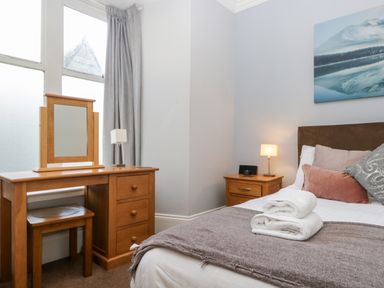A bedroom with a bed with pillows and towels beside a wooden dressing table and nightstand at Carlton House Apartment 1 in Keswick