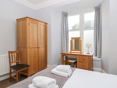 A bedroom with a wooden wardrobe chair and dressing table with mirror at Carlton House Apartment 1 in Keswick