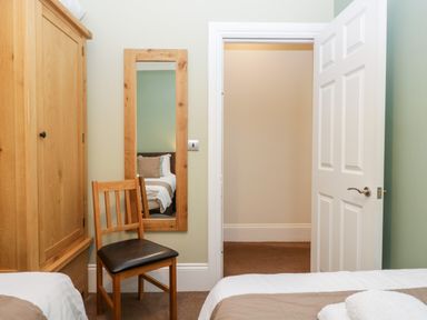 A bedroom with a wooden chair a wardrobe a wall mirror and an open door showing a hallway at Carlton House Apartment 1 Keswick