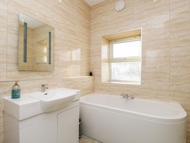A bathroom with a sink and cabinet beside a bathtub under a window at Carlton House Apartment 1 in Keswick