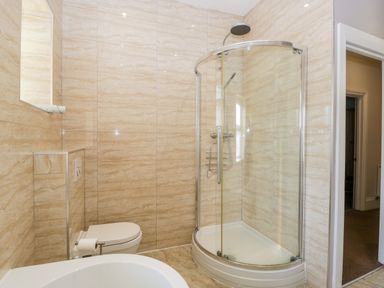 A bathroom with a curved glass shower, a toilet with a toilet paper holder, and tiled walls at Carlton House Apartment 1 in Keswick