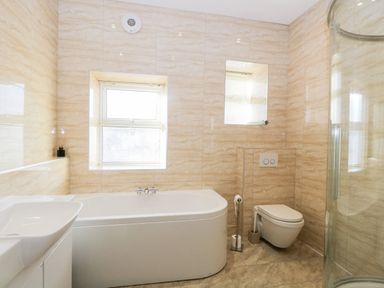 A bathroom with a bathtub a wall-mounted toilet a sink and a glass shower enclosure at Carlton House Apartment 1 in Keswick