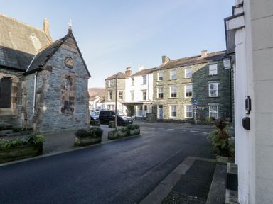 A street with parked cars and stone buildings including a church and residential houses at Carlton House Apartment 1 in Keswick