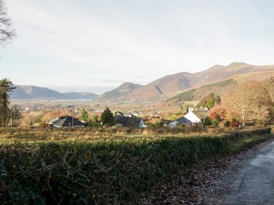 A rural landscape with houses trees hedges a road and mountains in the background at Carlton House Apartment 1 in Keswick