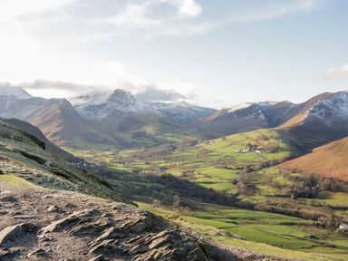 A valley with green fields and scattered houses surrounded by mountains with some snow at Carlton House Apartment 1 Keswick