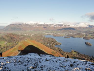 A mountainous landscape with snow patches overlooking a lake with islands and a valley at Carlton House Apartment 1 in Keswick