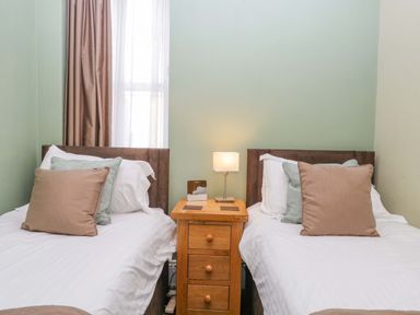 A bedroom with two single beds separated by a wooden nightstand with a lamp at Carlton House Apartment 1 in Keswick