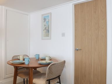 A dining area with round wooden table set with plates and mugs and two chairs near wooden and white doors at Harbour Studio in Sennen Cove
