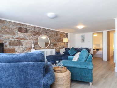 A living room with blue sofas a round mirror on a white cabinet and a stone wall at Harbour Studio in Sennen Cove