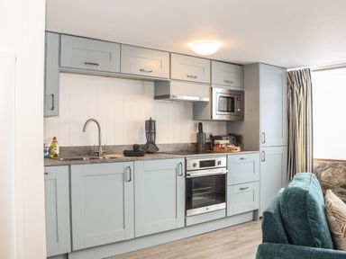 A kitchen with grey cabinets stainless steel appliances and a teal sofa at Harbour Studio in Sennen Cove