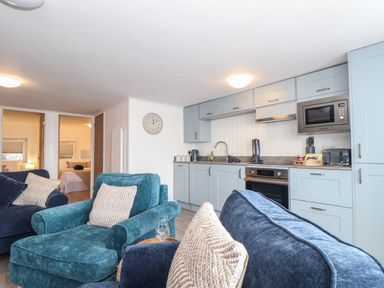 A kitchen with light blue cabinets and a living area with blue armchairs and pillows at Harbour Studio in Sennen Cove