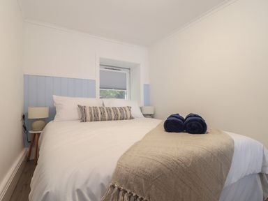A bedroom with a double bed bedside tables with lamps and a small window at Harbour Studio in Sennen Cove